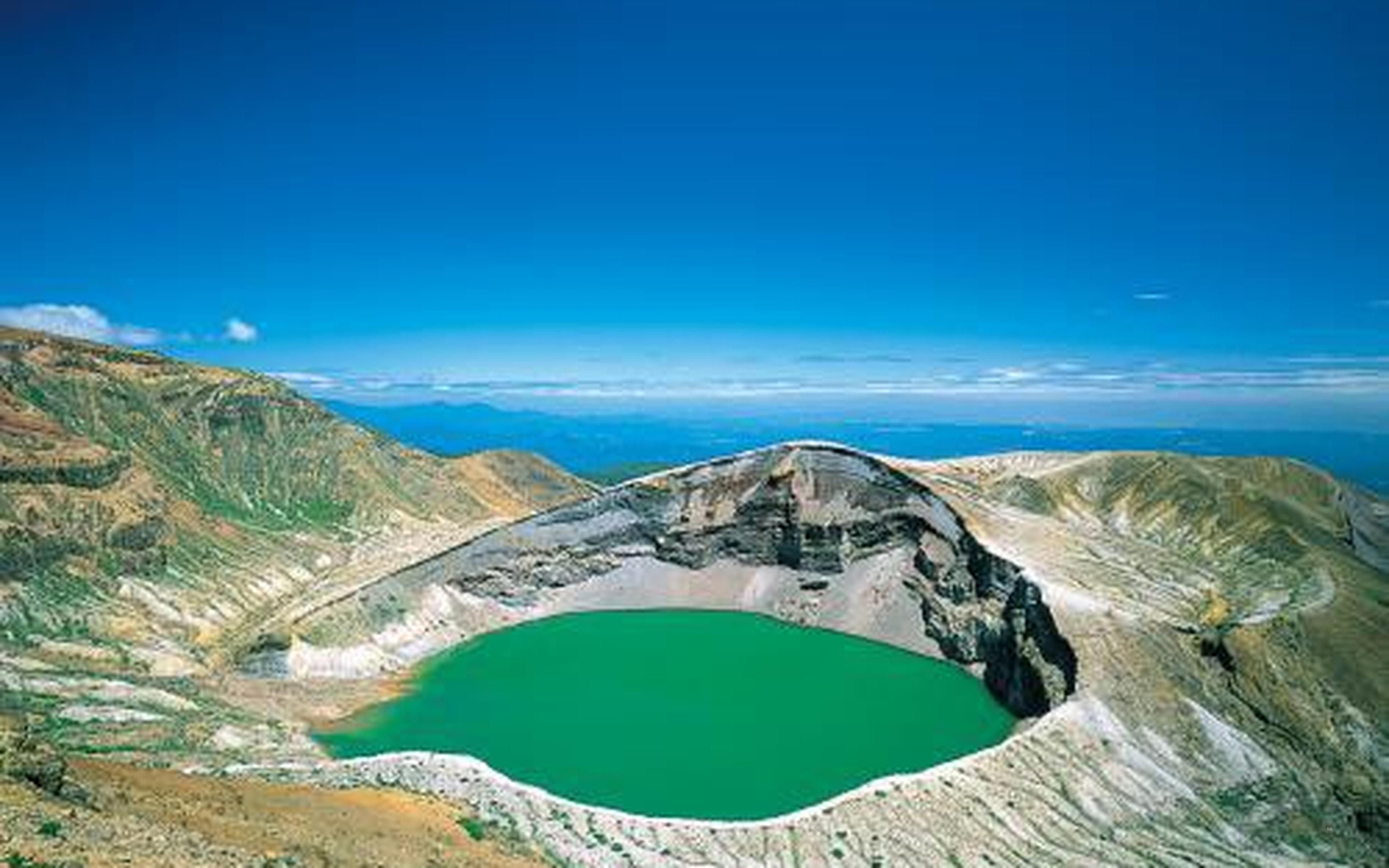 A round crater lake of green water inside rugged crater walls
