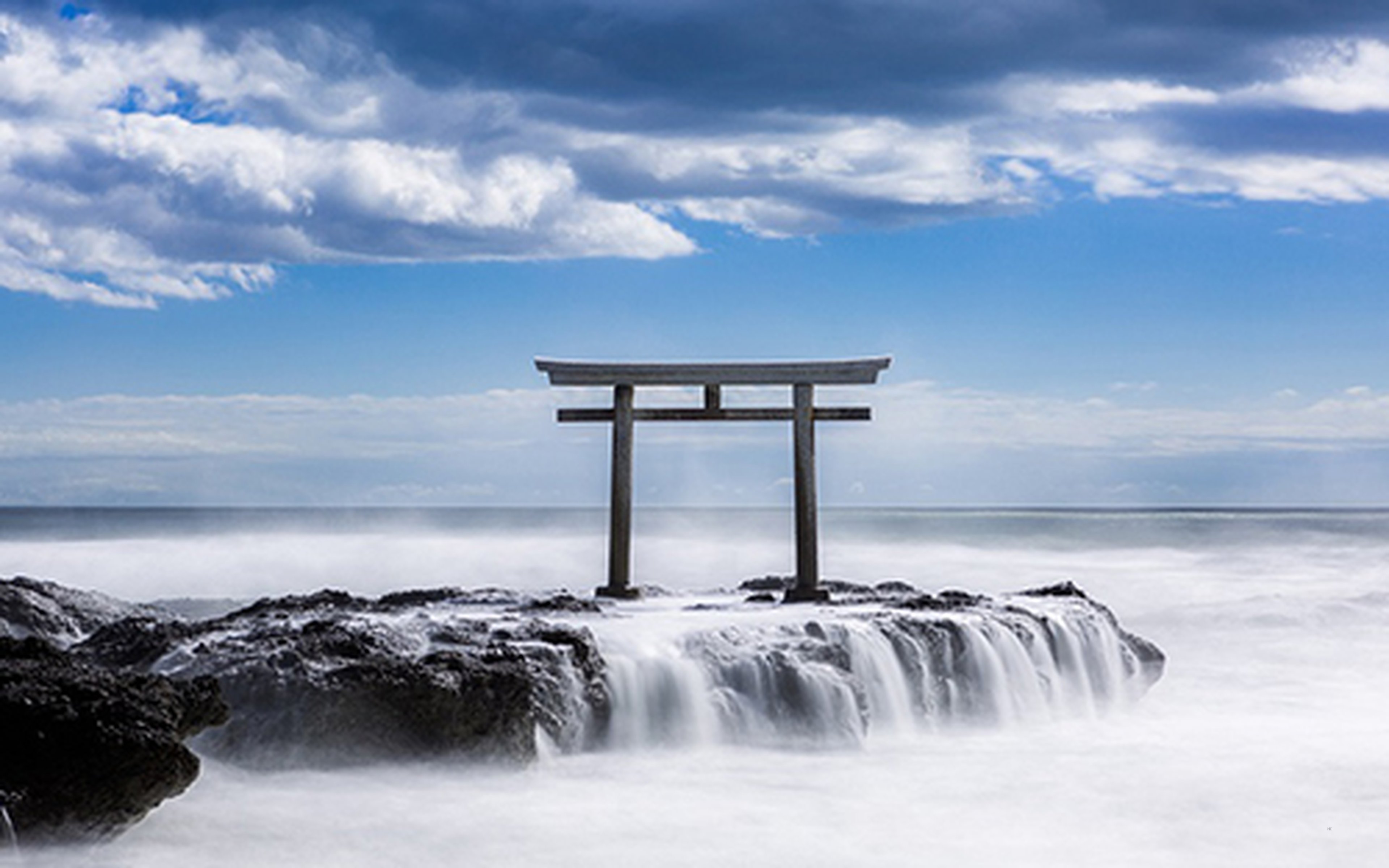 A torii gate standing on rocks in crashing waves