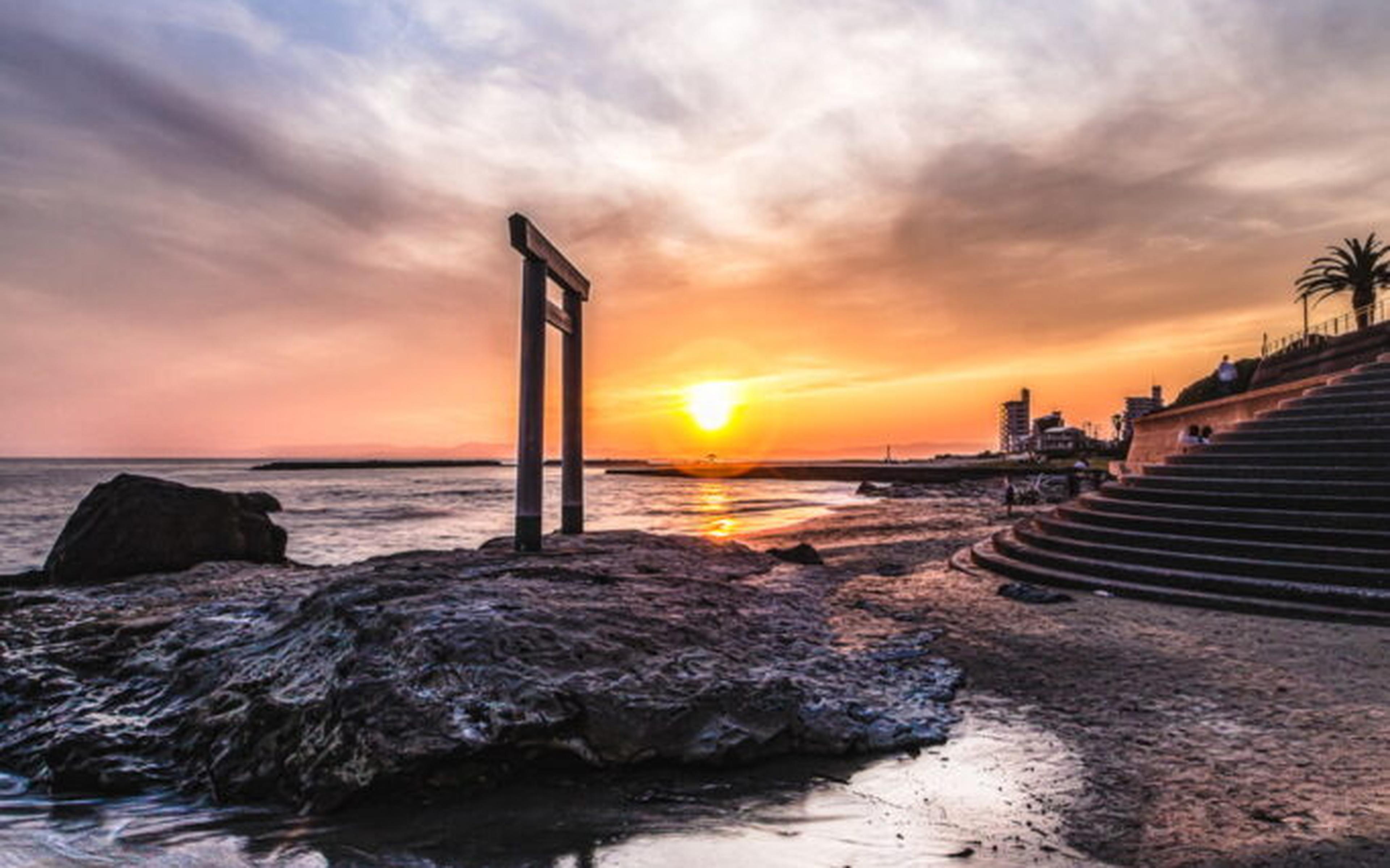 A torii gate on the shoreline at sunset near the coast