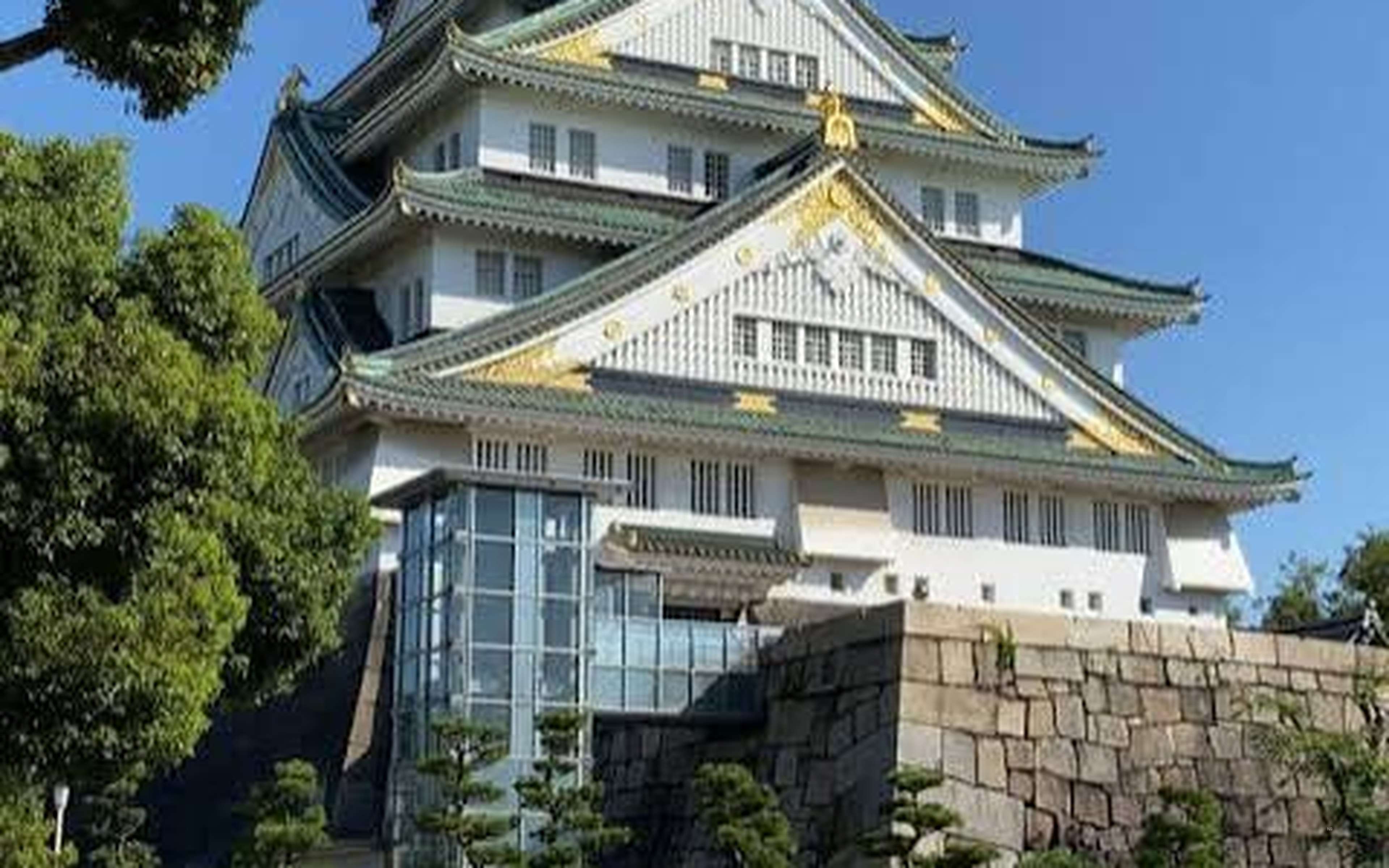 Blue sky over the main keep of Osaka Castle, with stone walls and pine trees in the foreground