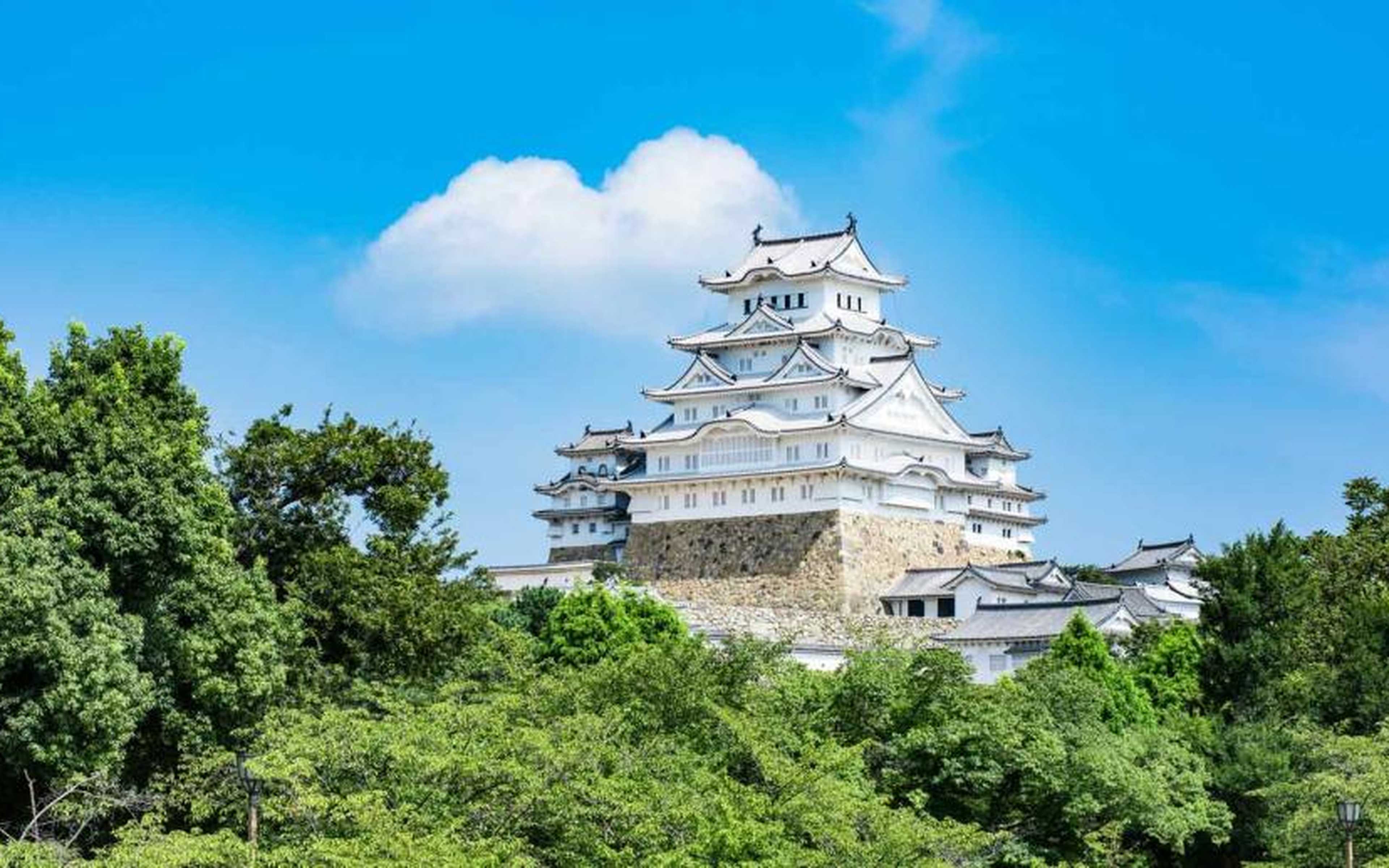 Himeji Castle's white main keep surrounded by greenery under a clear blue sky